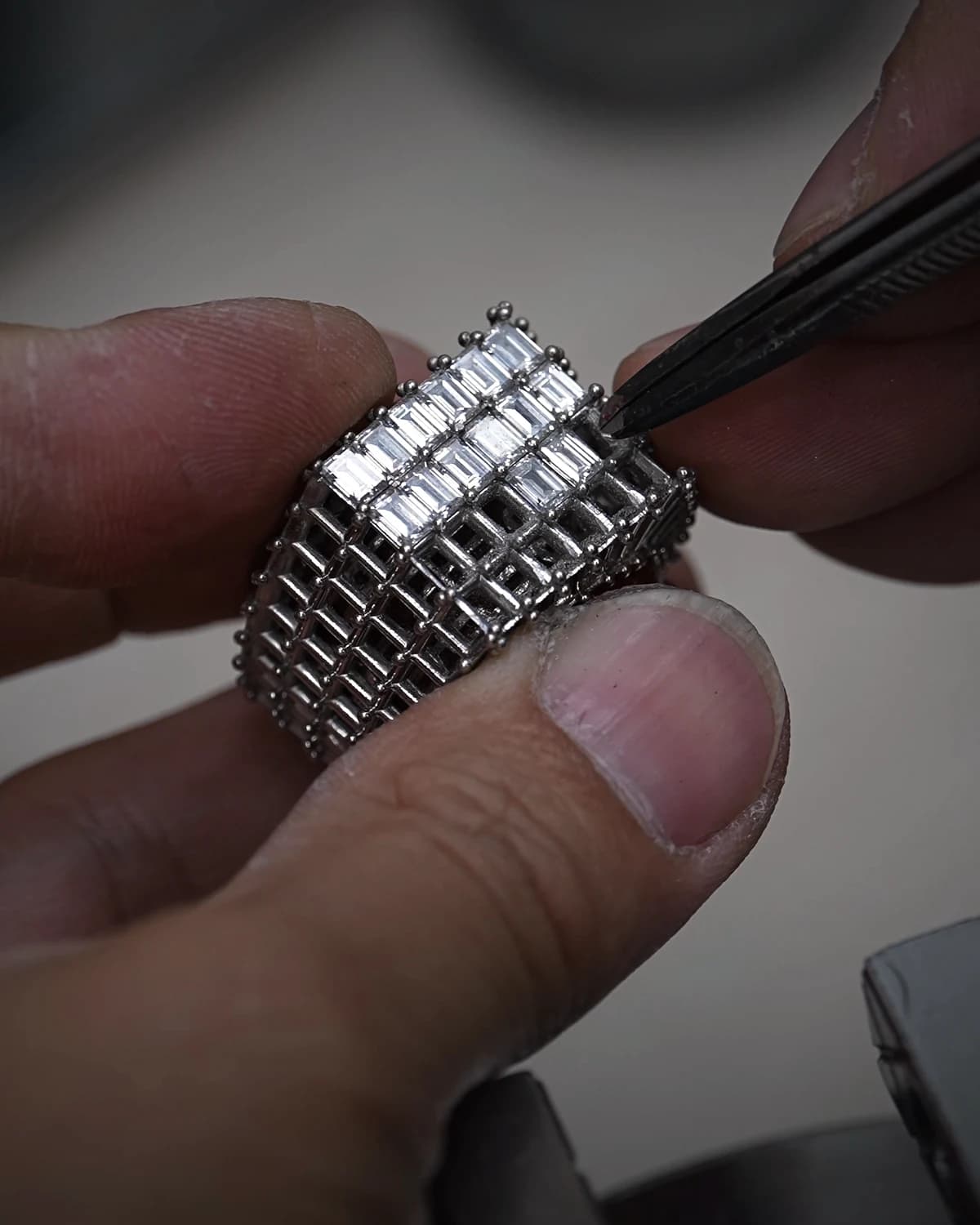 An artisan's hands setting a stone into a baguette-cut eternity ring with tweezers